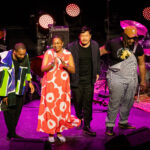Cécile McLorin Salvant in een rood-witte bloemenjurk applaudisseert op het podium van Kongsberg Jazzfestival 2024, naast haar band