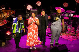 Cécile McLorin Salvant in een rood-witte bloemenjurk applaudisseert op het podium van Kongsberg Jazzfestival 2024, naast haar band