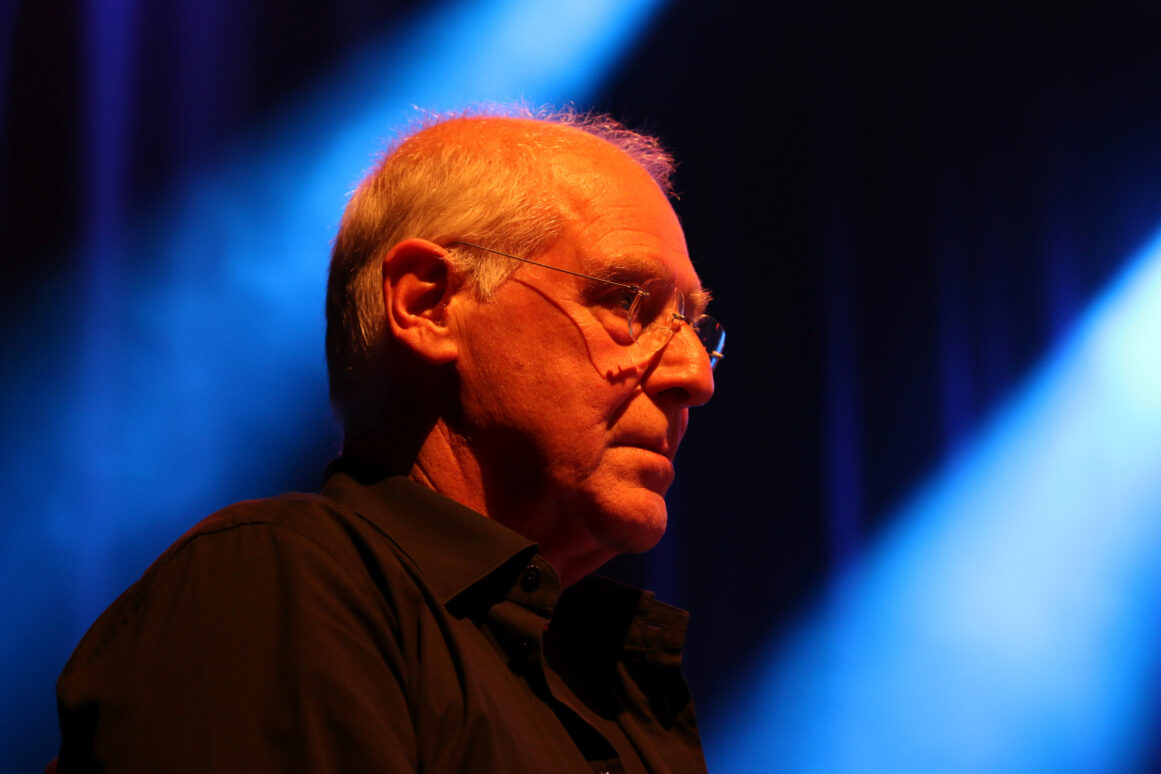 Michael Mantler, grijs haar en randloze bril, in profiel op het podium voor blauw licht (Deutsches Jazzfestival Frankfurt, 2015).